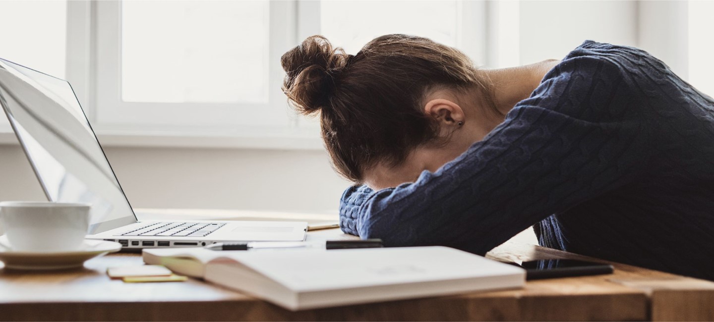 Stock photo of an exhausted person resting her head on a desk.