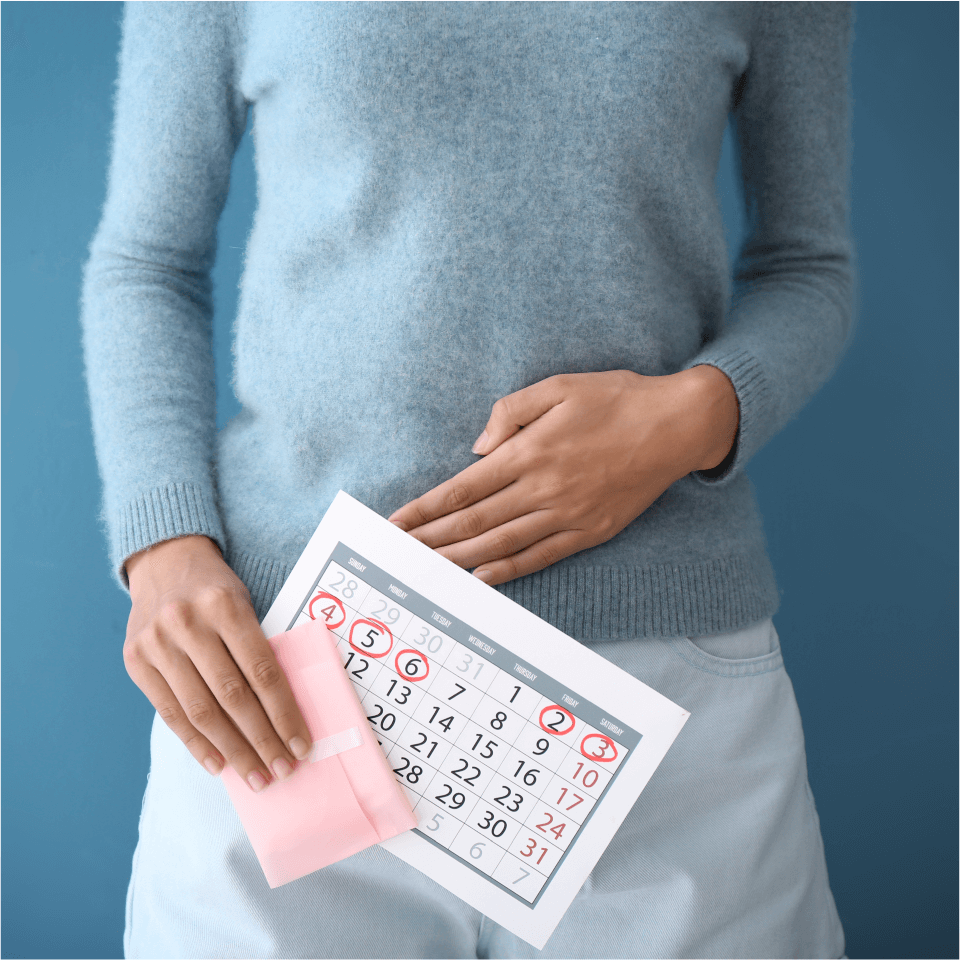 Woman touching her abdomen while holding a calendar and a sanitary napkin.