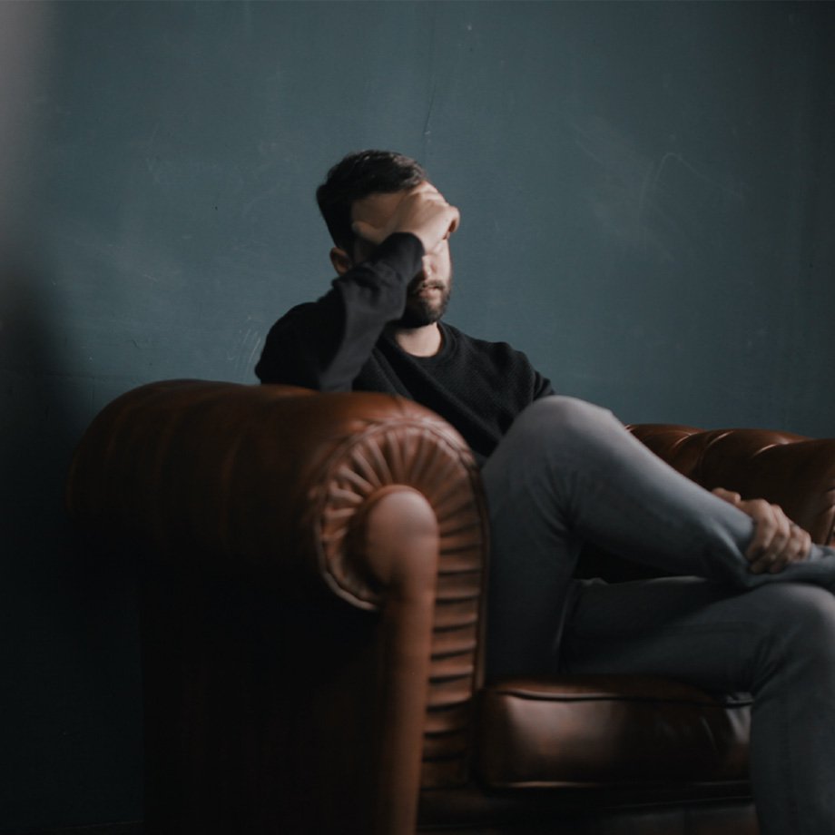 Person sitting on an armchair, touching his head.