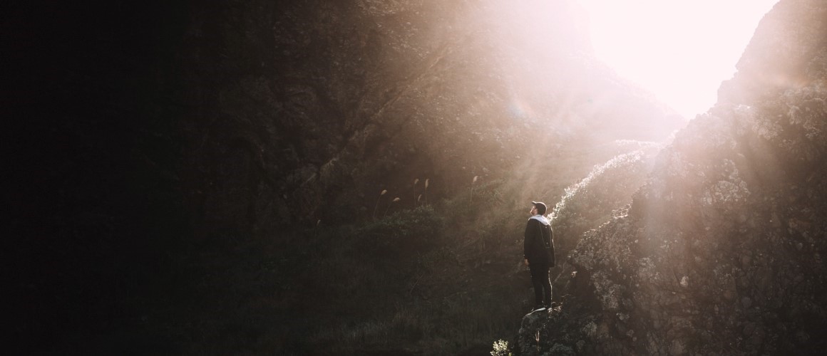 Stock photo of a hiker on a mountain looking up at the ray of sunbeam shining through.