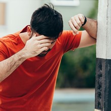 Stock photo of a person leaning against a wall, touching their head.